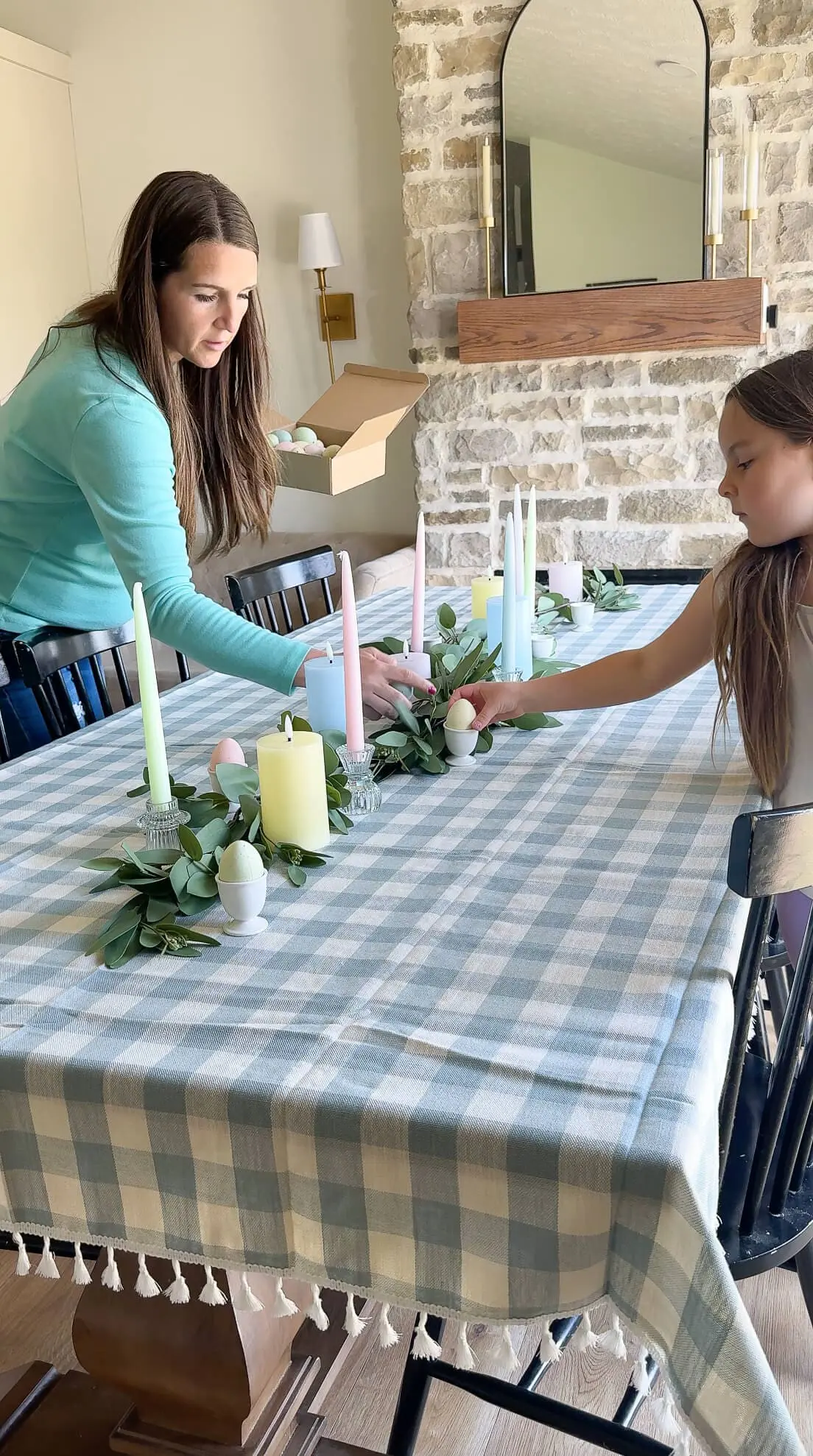Pastel egg decorations being added to a soft eucalyptus garland centerpiece as part of Easter table decor.